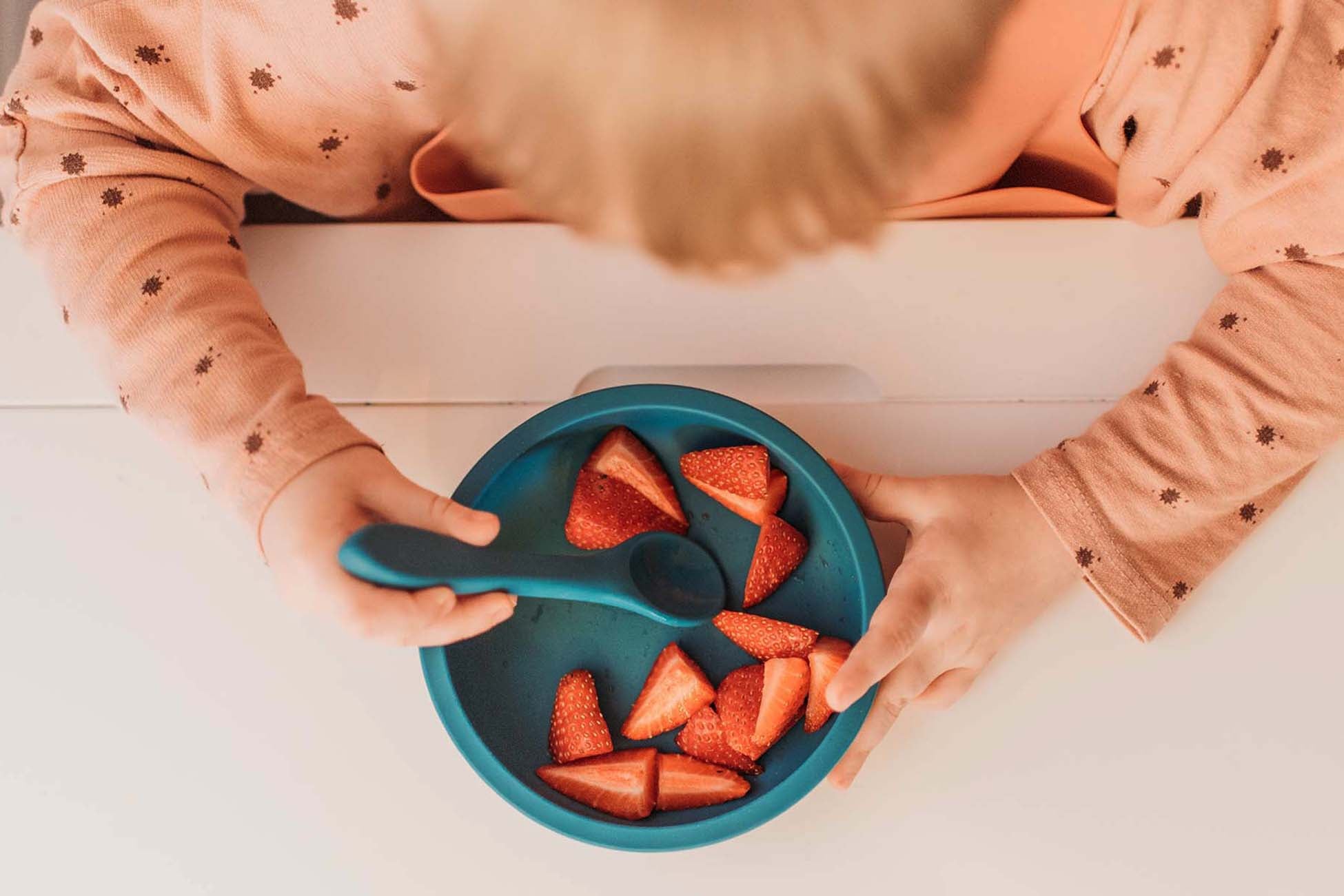 Baby holding mini utensil over bowl